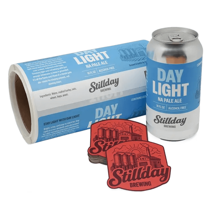 Roll of custom brewery can labels beside a labeled aluminum beer can and stacked Stillday Brewing die cut stickers on a white background.