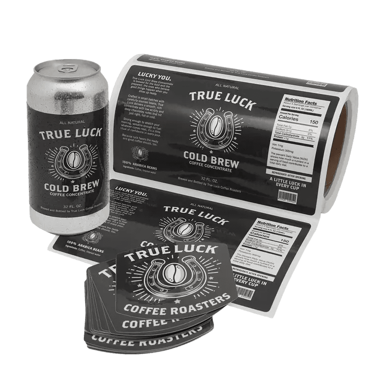 Custom cold brew coffee can label beside a labeled beverage can, roll of coffee labels, and stacked True Luck Coffee Roasters stickers on a white background.