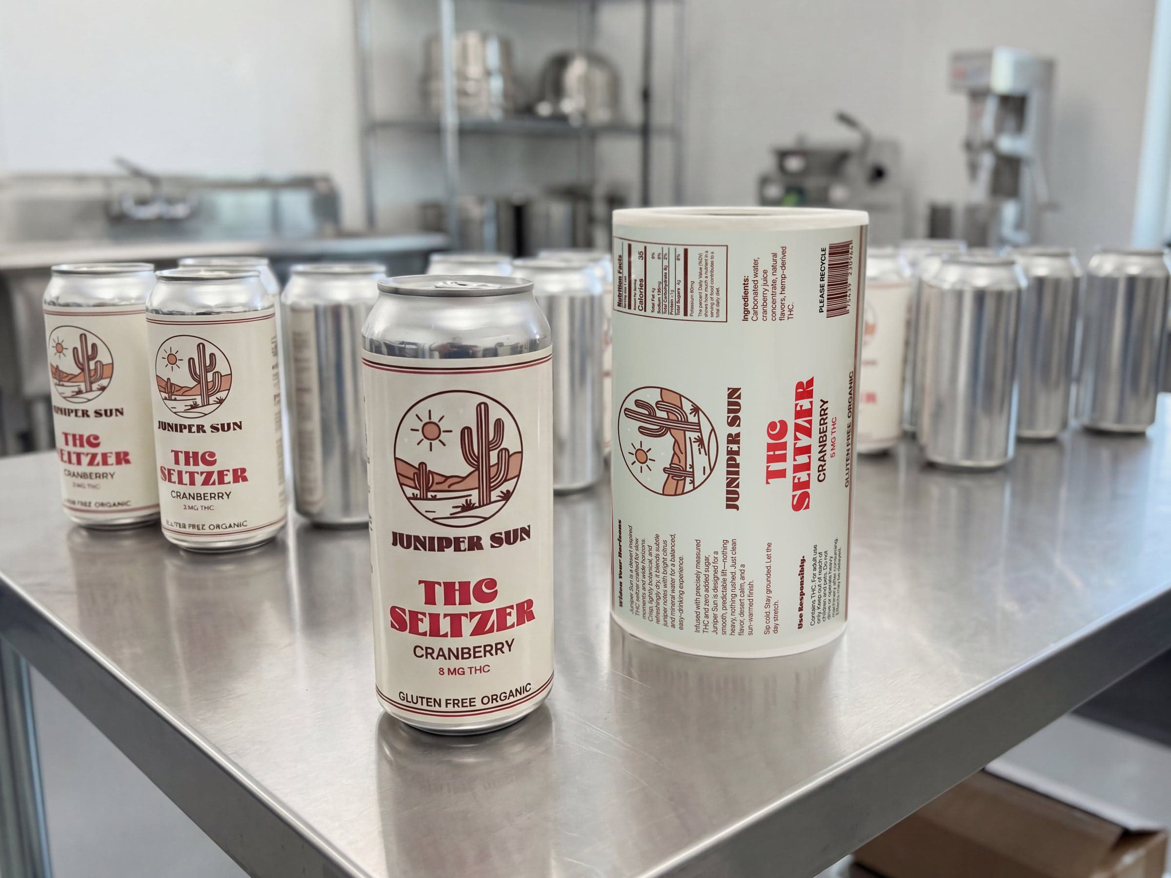THC seltzer cans and printed beverage label roll displayed on a production table for cannabis beverage packaging.