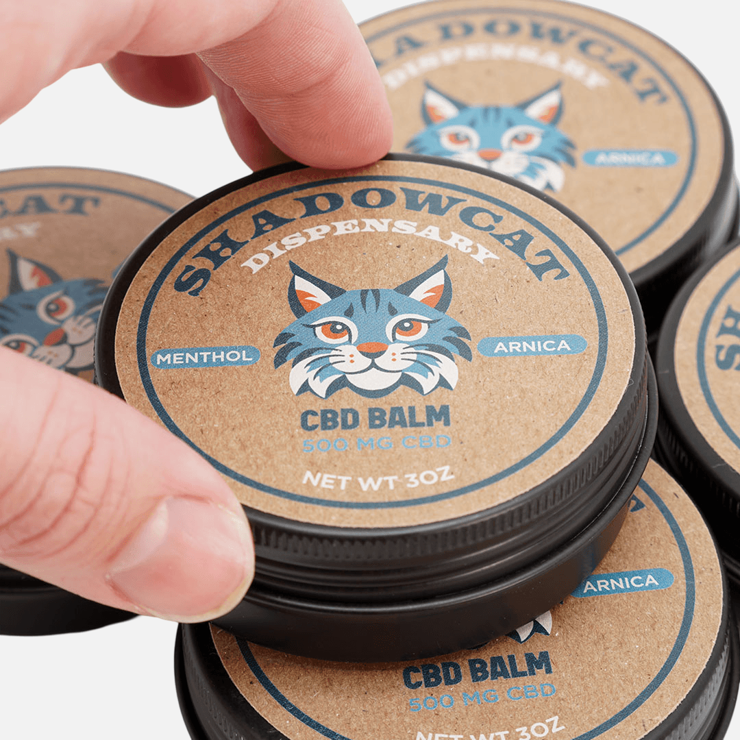 Custom kraft paper labels applied to CBD balm tins with a matte natural finish.