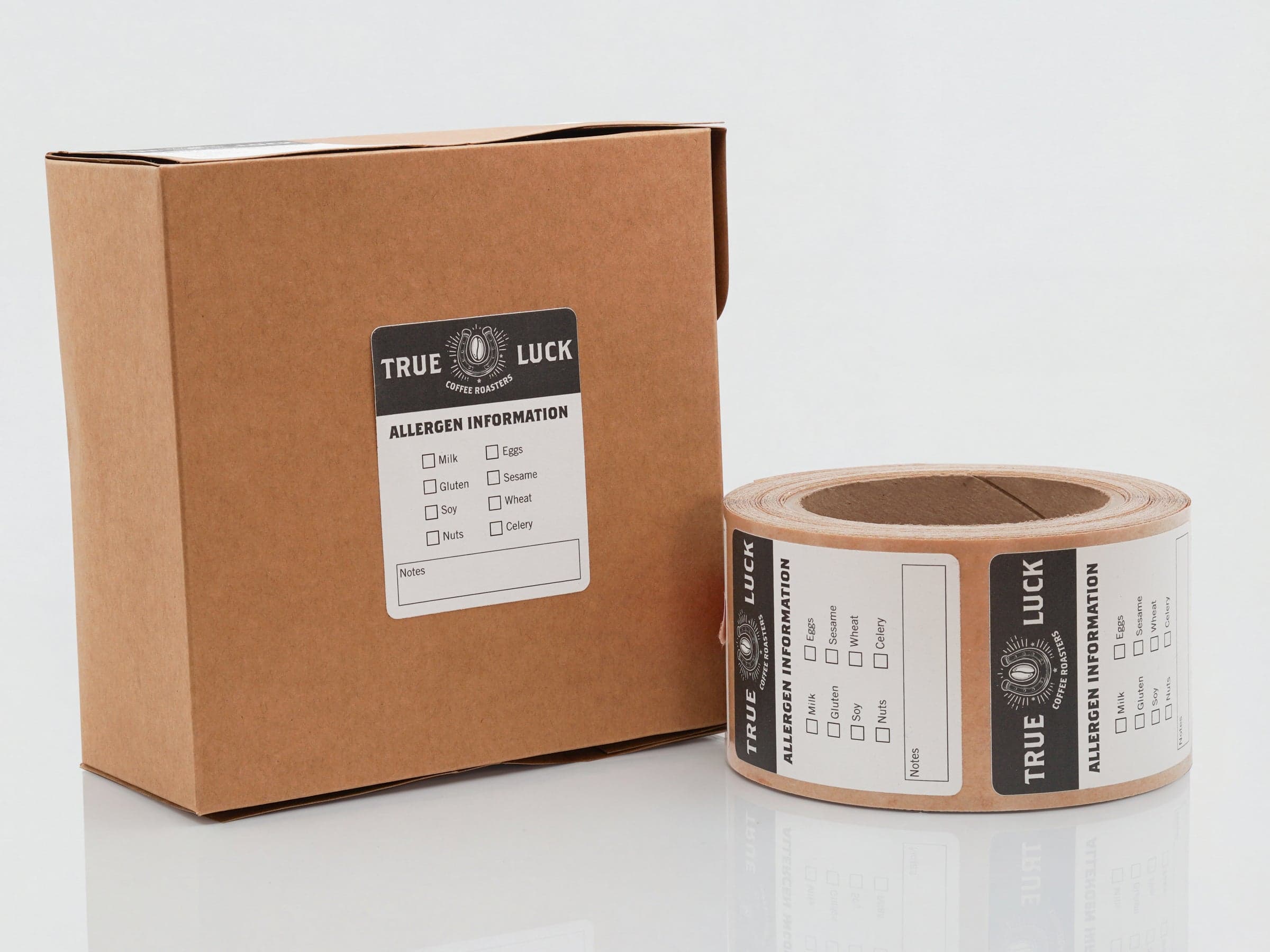 Custom food packaging labels on a cardboard shipping box and label roll featuring allergen information for product packaging.