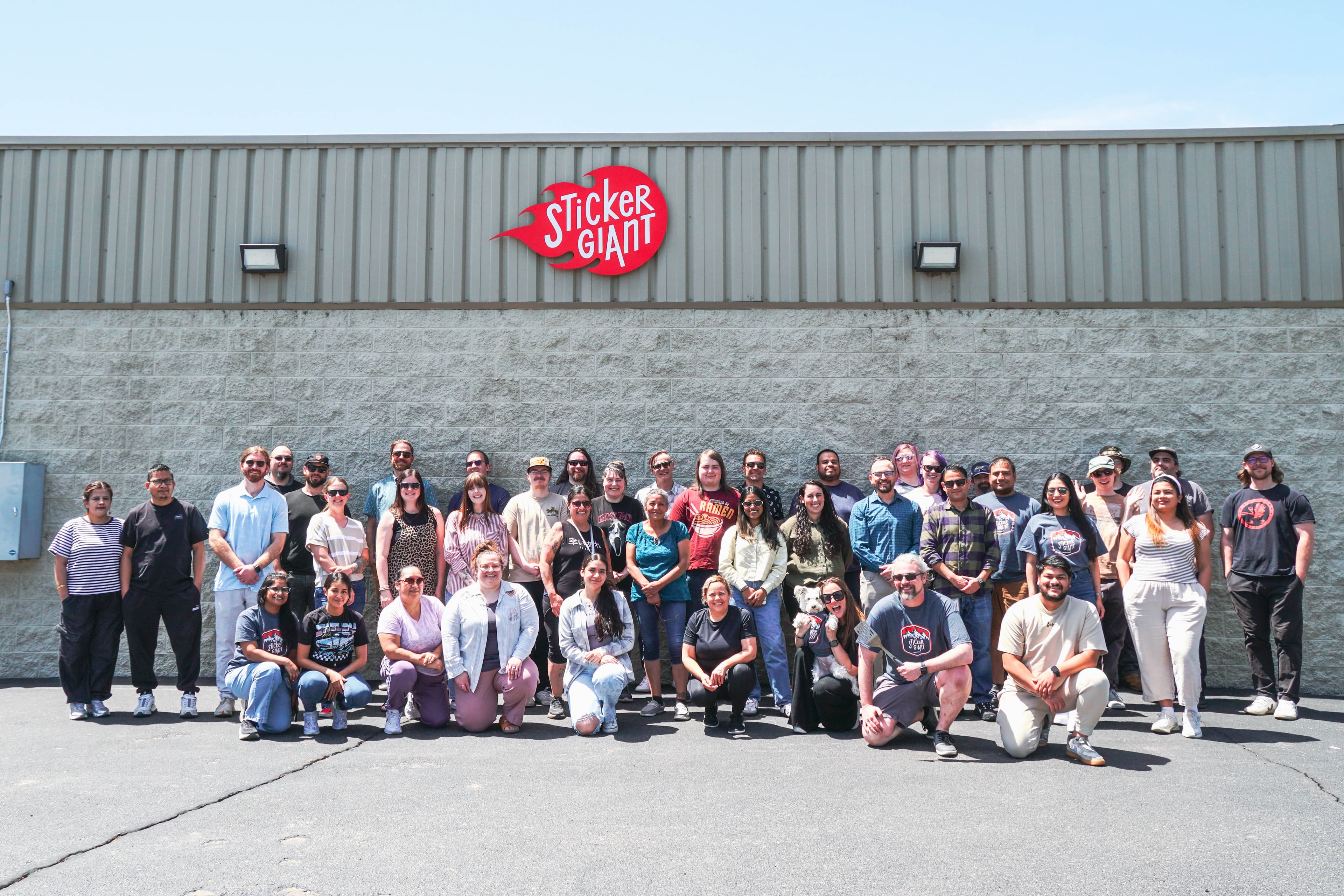 Sticker Giant team members gathered outside the company’s Longmont, Colorado printing facility beneath the Sticker Giant building sign.