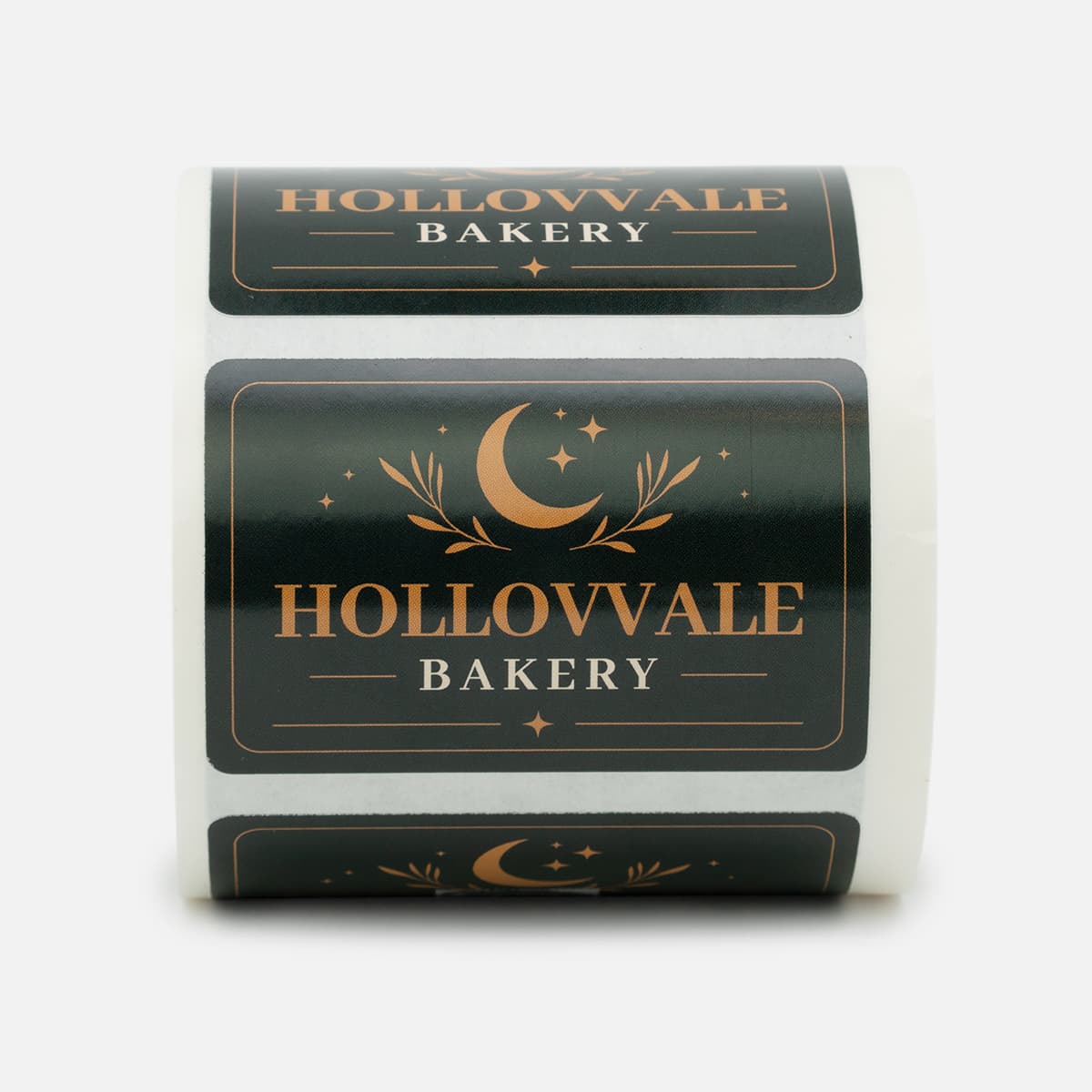 Roll of custom Hollowvale Bakery labels featuring black and copper artwork with a crescent moon and star design.