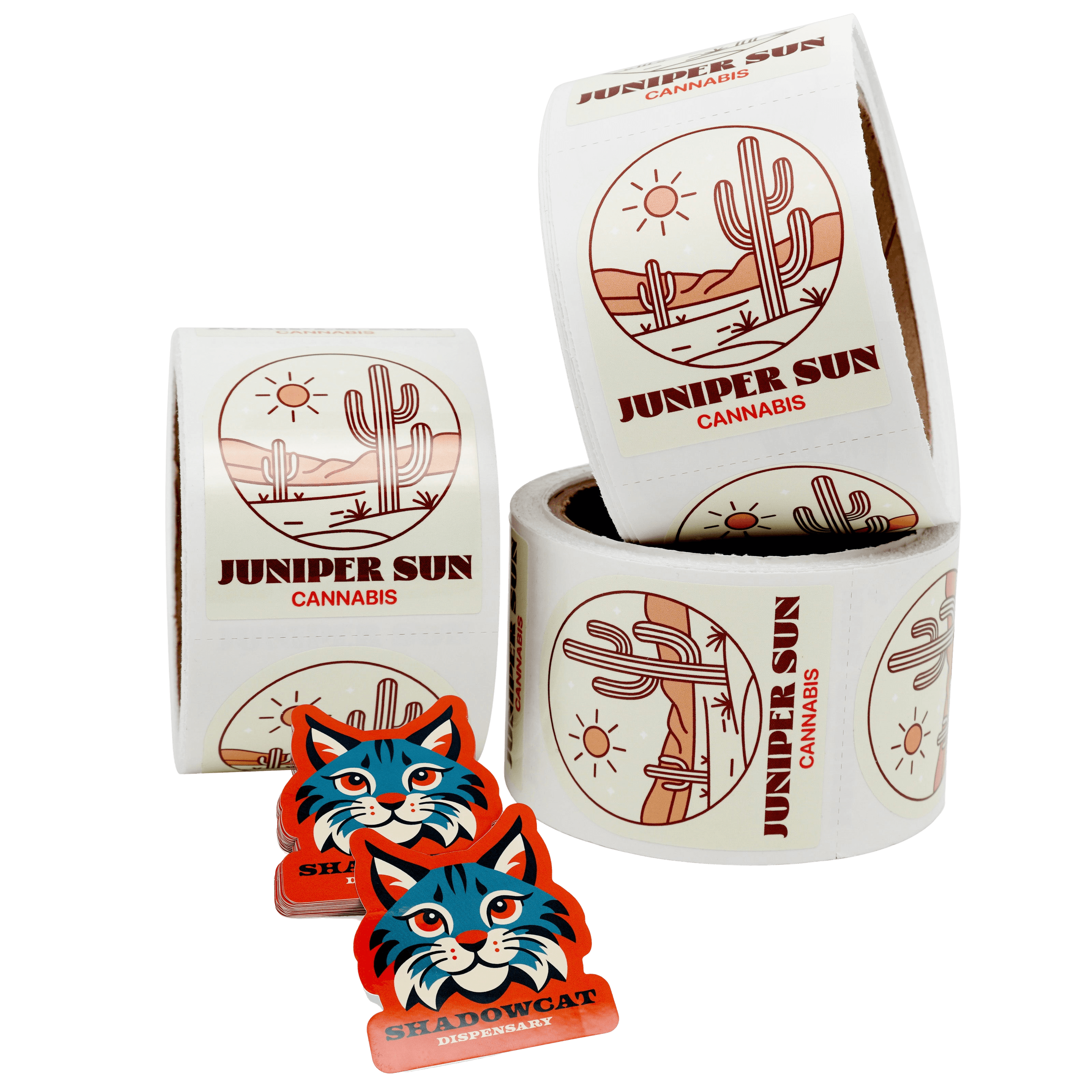 Rolls of custom cannabis product labels featuring a desert cactus design beside stacked die cut “Shadowcat Dispensary” stickers on a white background.