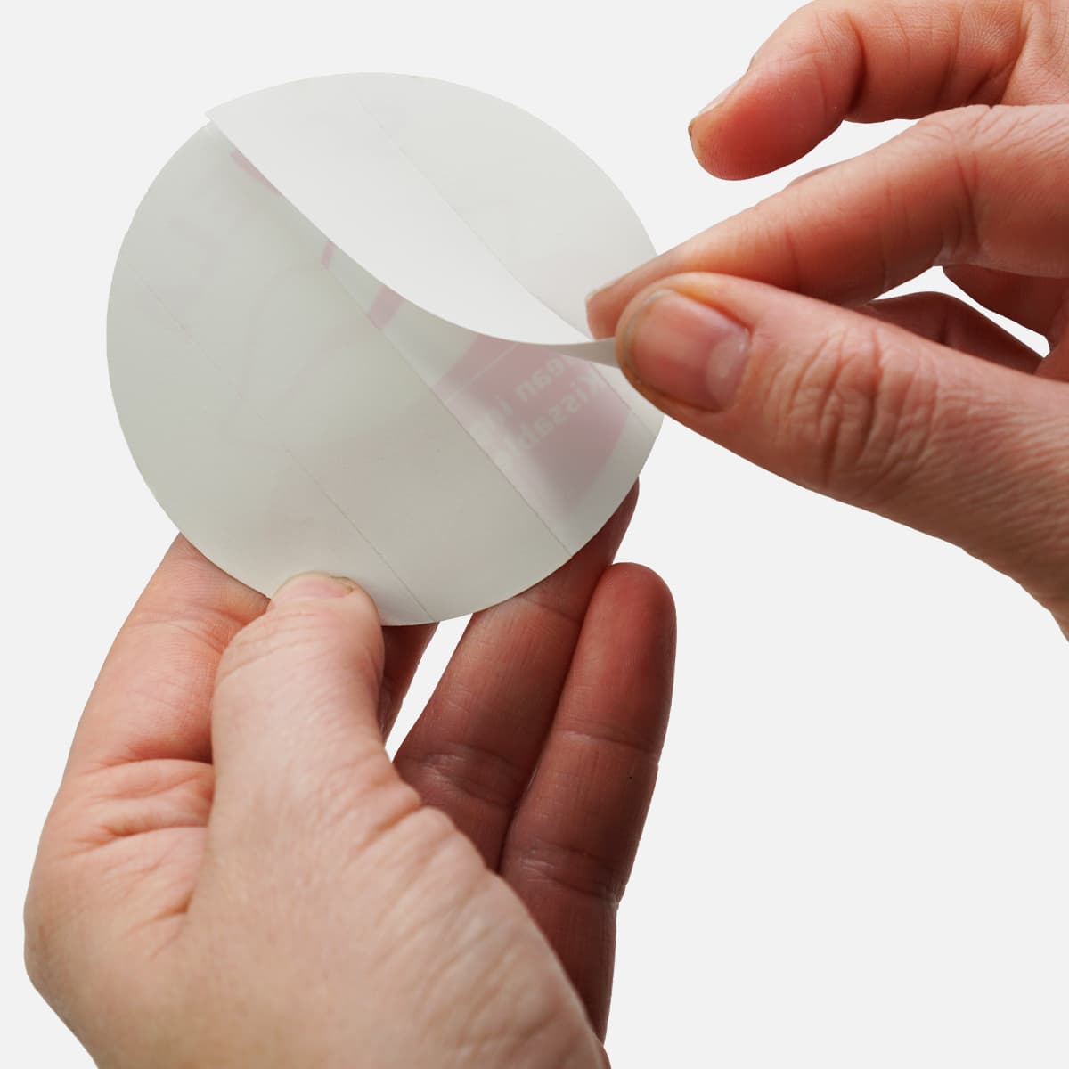 Close-up of hands peeling a round split-back sticker liner, demonstrating easy application and removal.