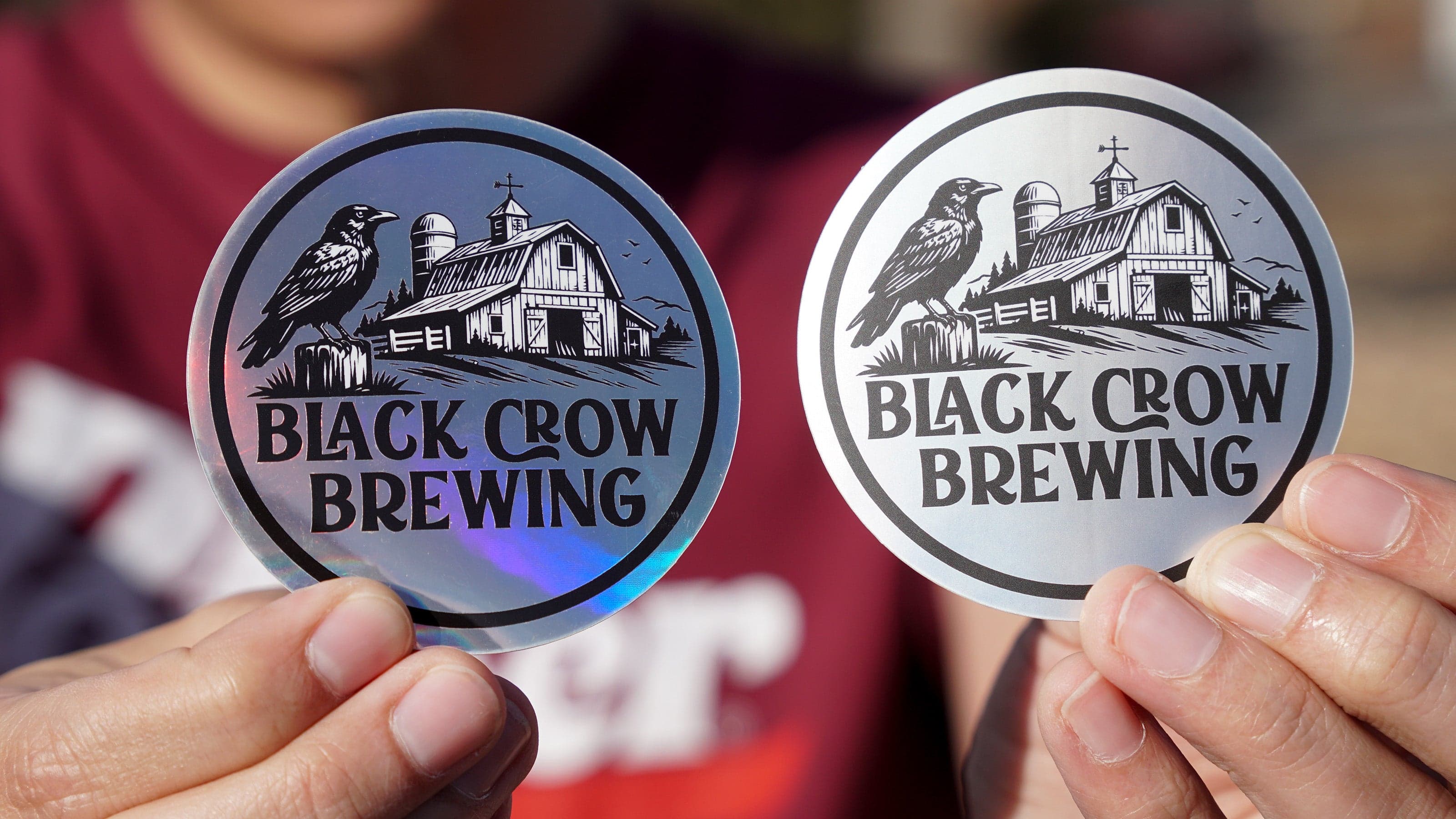 Matte holographic and glossy holographic brewery stickers held side by side, showing the difference in finish and light reflection on custom beer brand stickers.