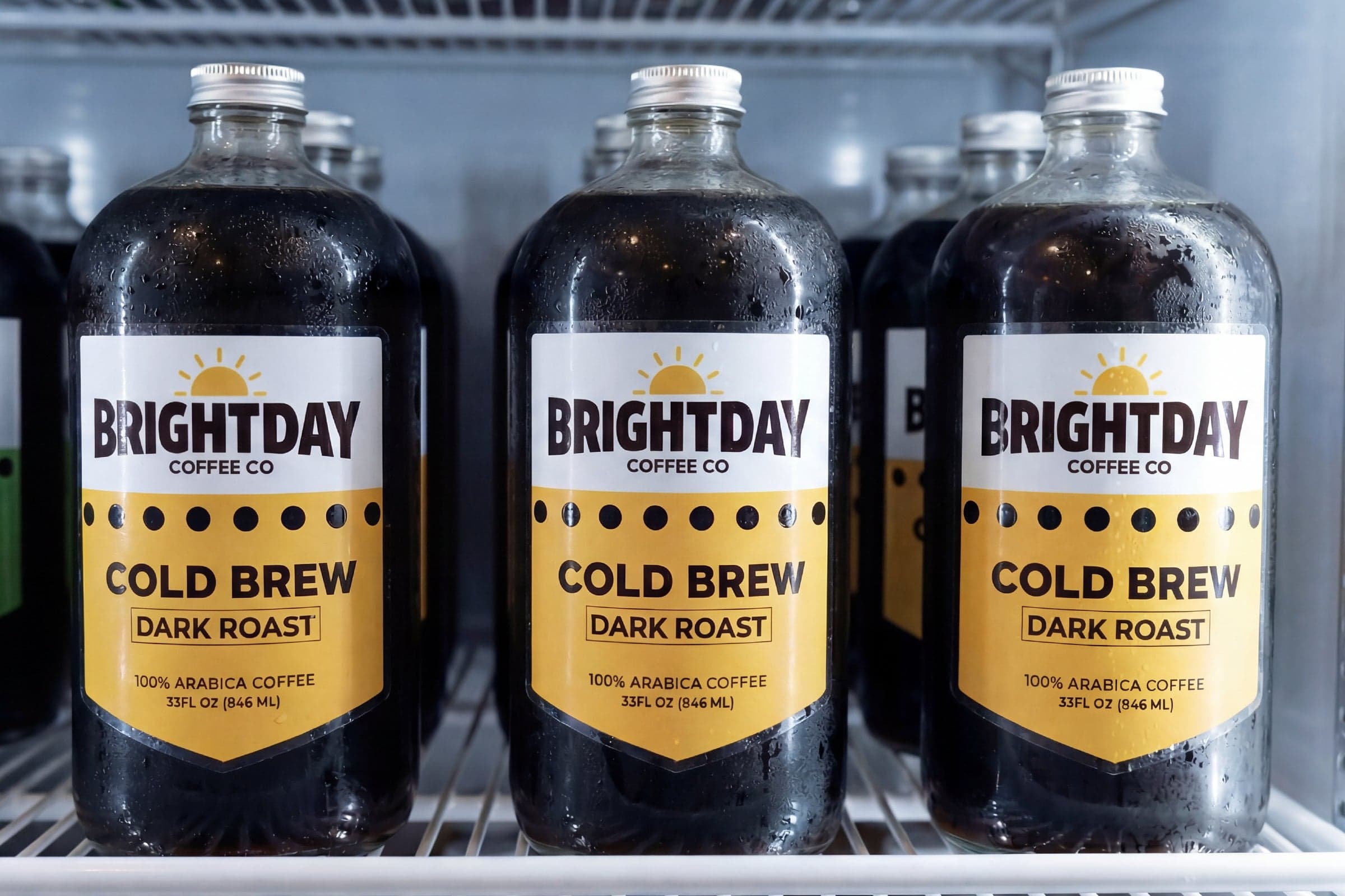 Cold brew coffee bottles with custom beverage labels displayed in a refrigerated retail cooler.